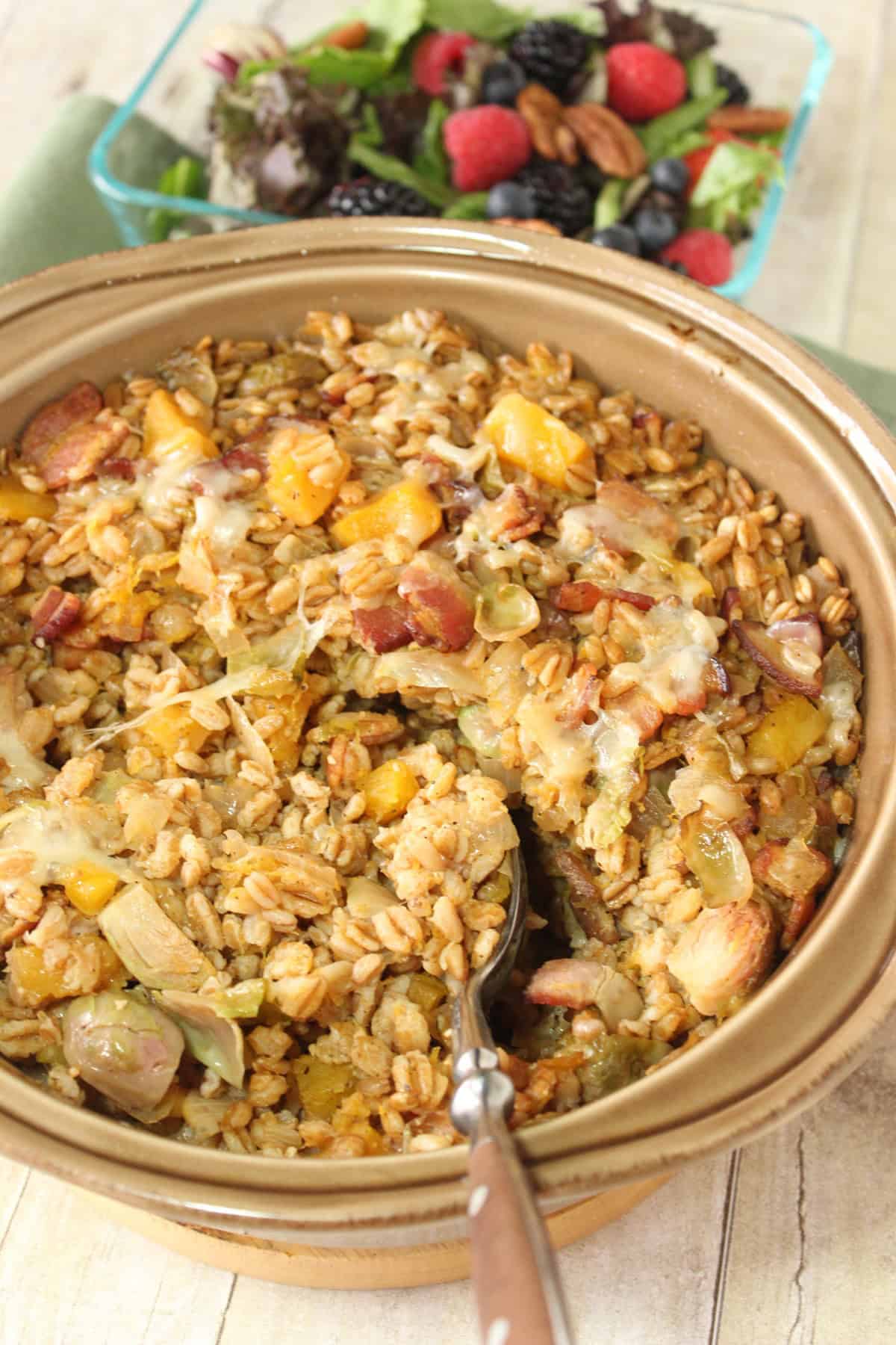 A baked farro casserole with a colorful salad in the background.