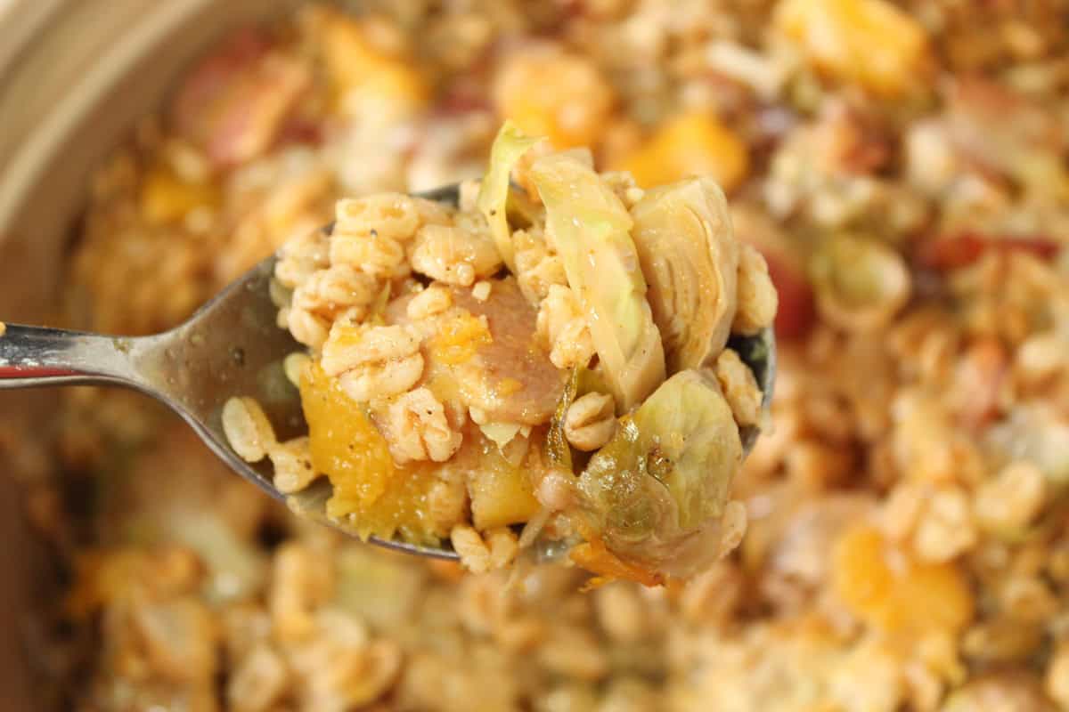 A spoon holding up a serving of farro casserole with Brussels sprouts and butternut squash.