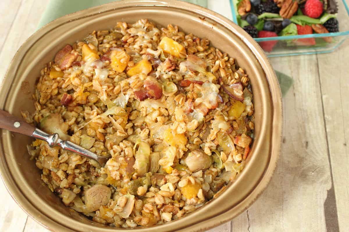 Baked Farro Casserole with Butternut Squash, Bacon and Brussels Sprouts is a deliciously savory dish with plenty of healthy whole grains and tons of texture and taste. - kudoskitchenbyrenee.com A round ceramic baking dish filled with baked farro casserole with butternut squash, Brussels sprouts and bacon.