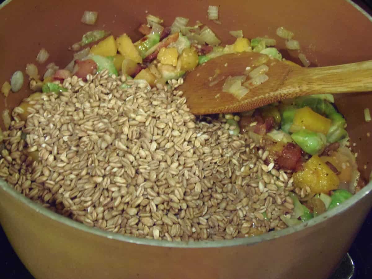 Raw farro in a stockpot with butternut squash and Brussels sprouts.