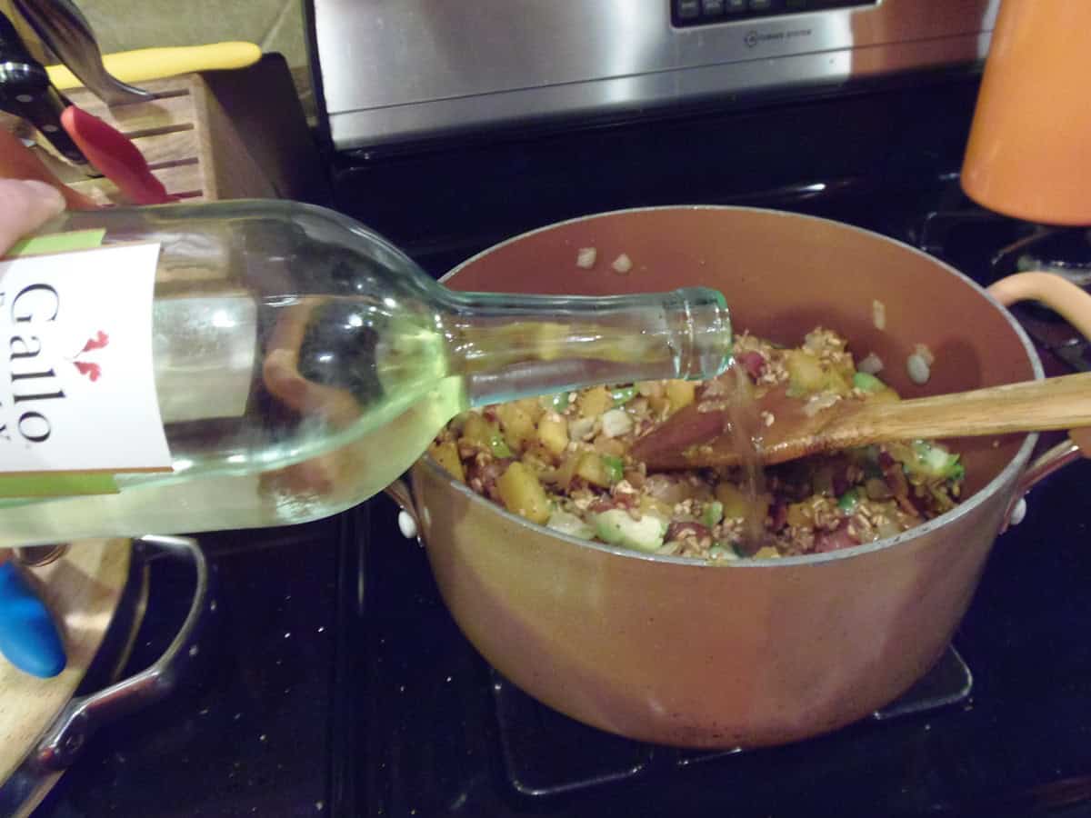 White wine being added into a pot on the stovetop containing farro and veggies.