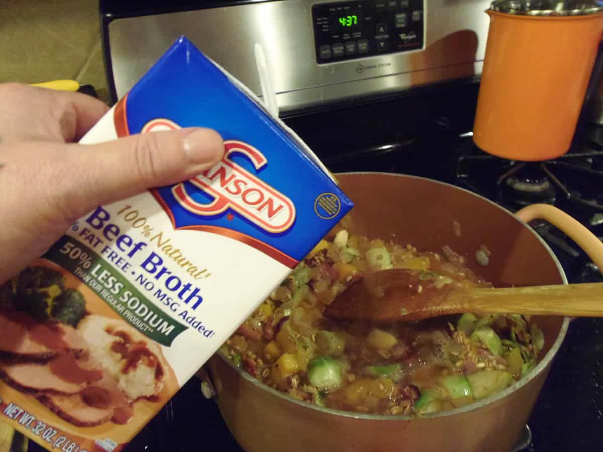 A carton of beef stock over a pot on the stovetop.