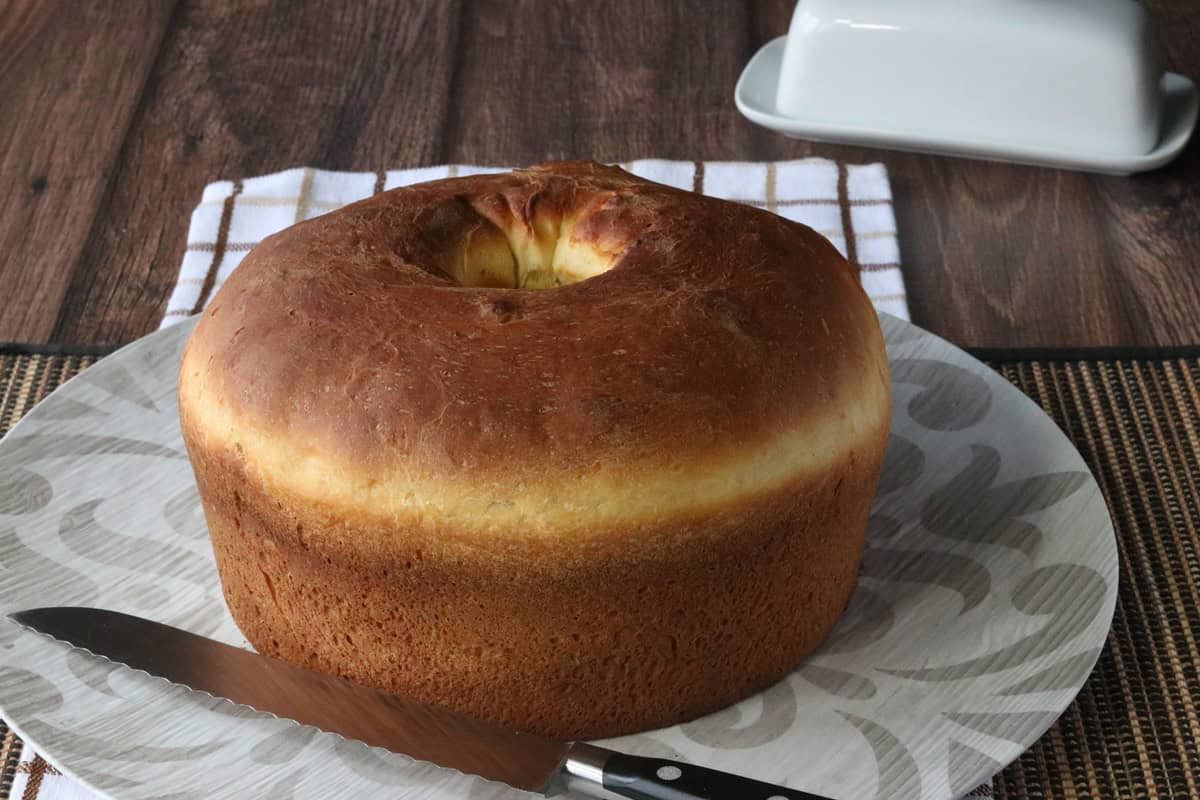 A round loaf of Sally Lunn Bread on a round platter with a serrated knife.