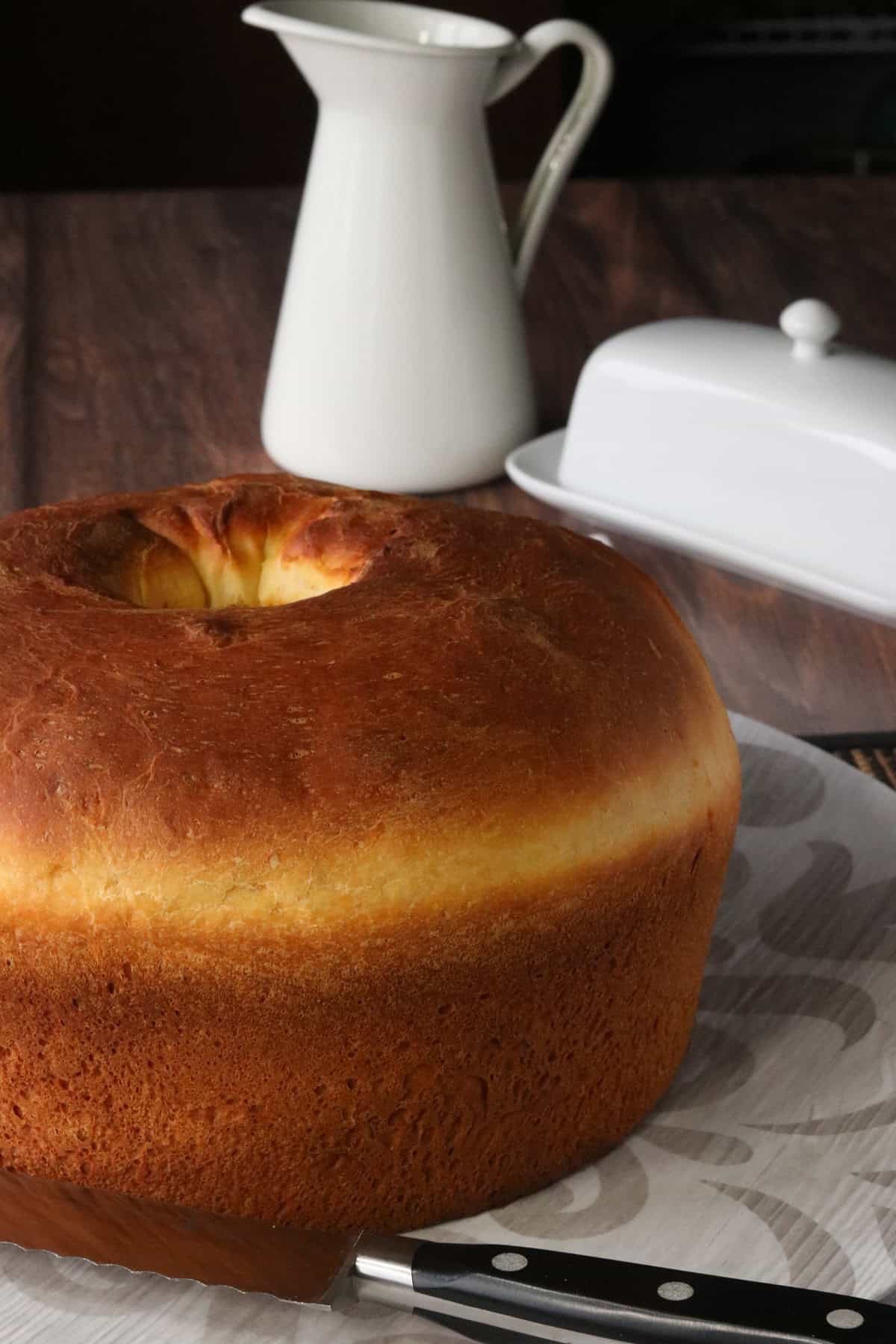 A beautiful round loaf of Sally Lunn bread with a butter dish and milk pitcher in the background.