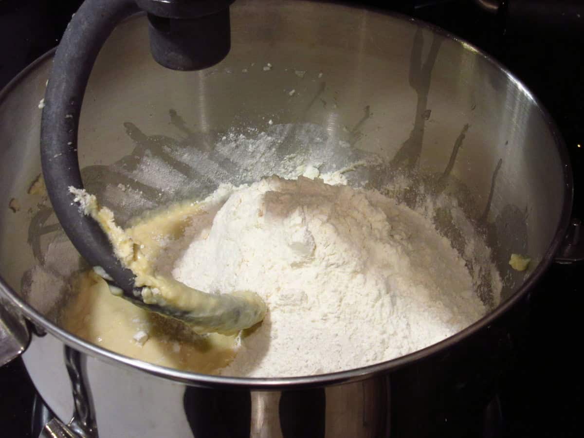 Additional flour being added to a sticky wet bread dough in a stand mixer bowl.