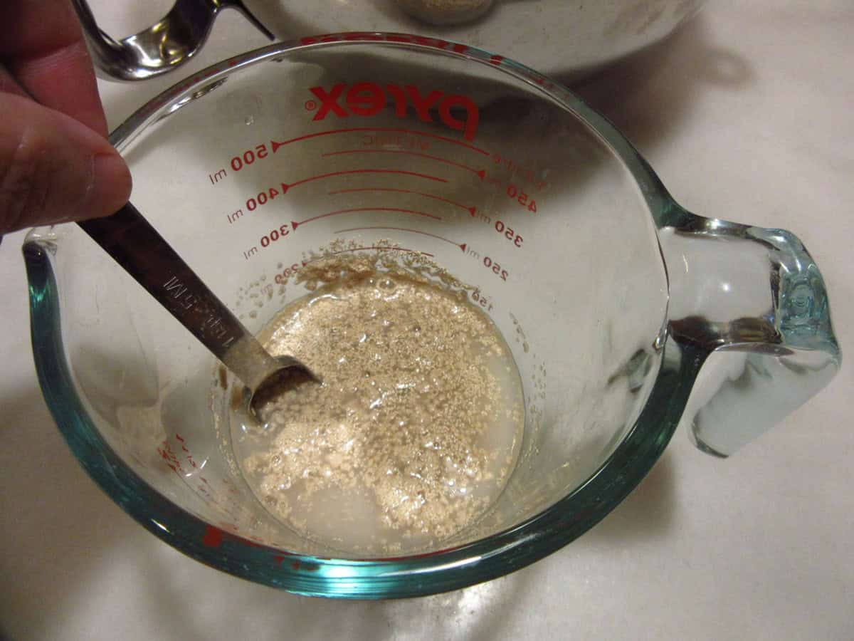 A spoon stirring active dry yeast and water in a measuring cup.
