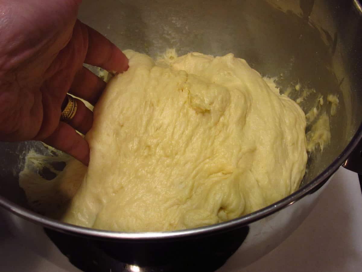 A hand deflating a soft Sally Lunn batter bread dough after proofing.
