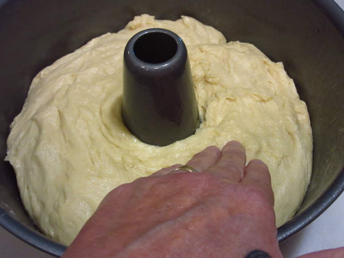 A hand smoothing a soft batter bread dough into a tube pan for baking.