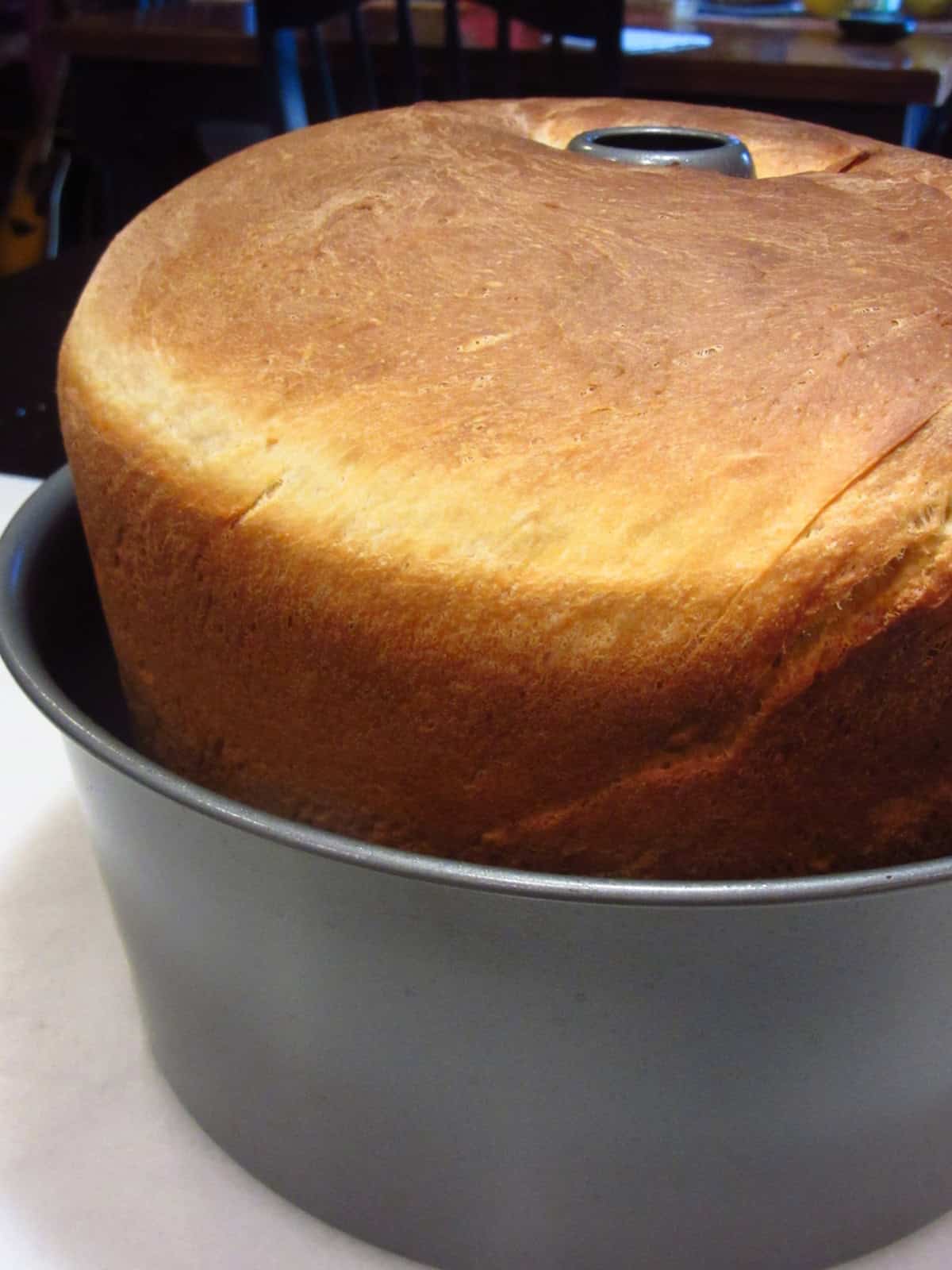 The sides of the tube pan being lowered from the bread for cooling the loaf.