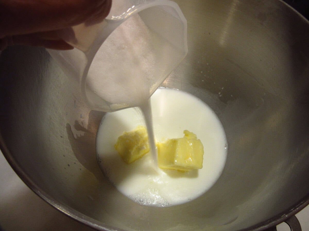 Milk being added to butter in a stand mixer bowl.