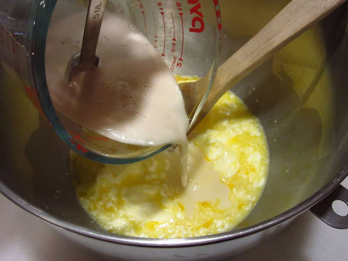 A yeast and water mixture being poured into a stand mixer with milk, eggs, and butter.