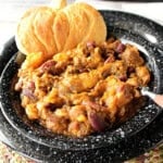 A black bowl filled with a serving of butternut squash chili and a pumpkin-shaped biscuit.