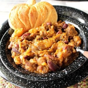 A black bowl filled with a serving of butternut squash chili and a pumpkin-shaped biscuit.