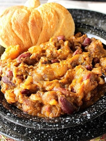 A black bowl filled with a serving of butternut squash chili and a pumpkin-shaped biscuit.