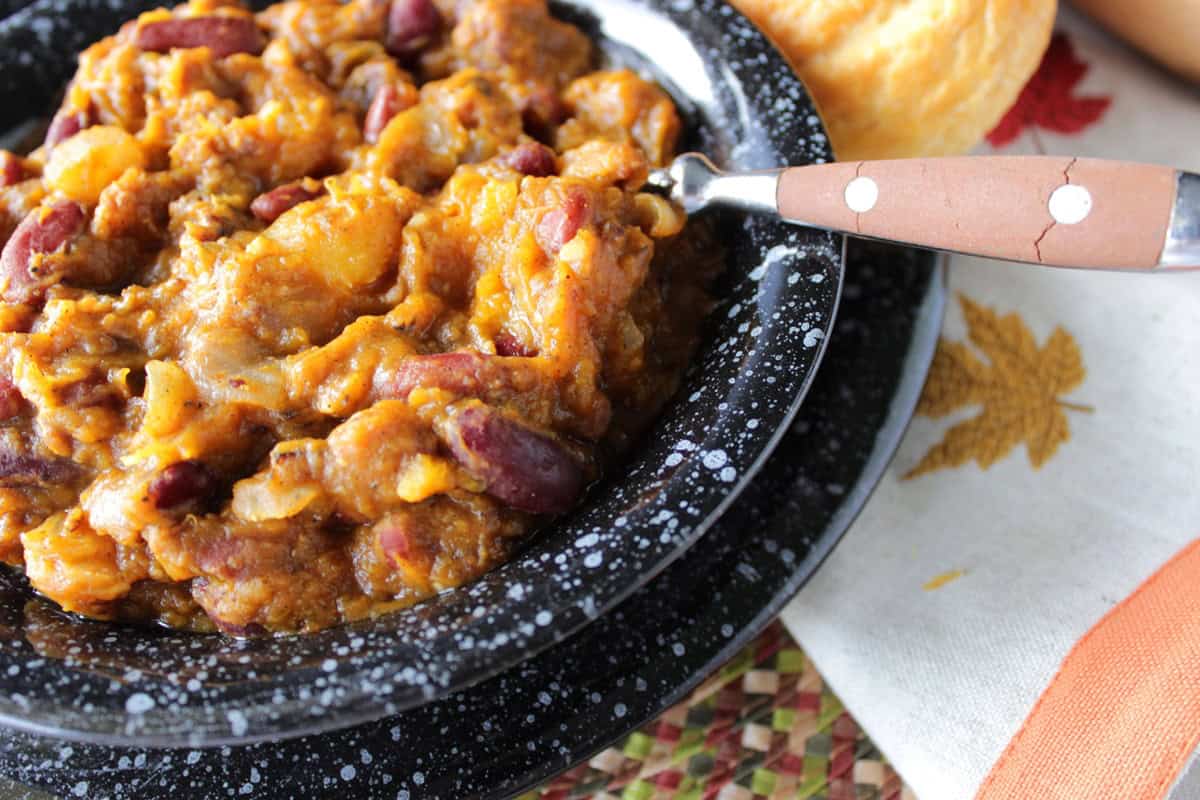 Dark and light red kidney beans along with butternut squash chili in a black bowl with a spoon.