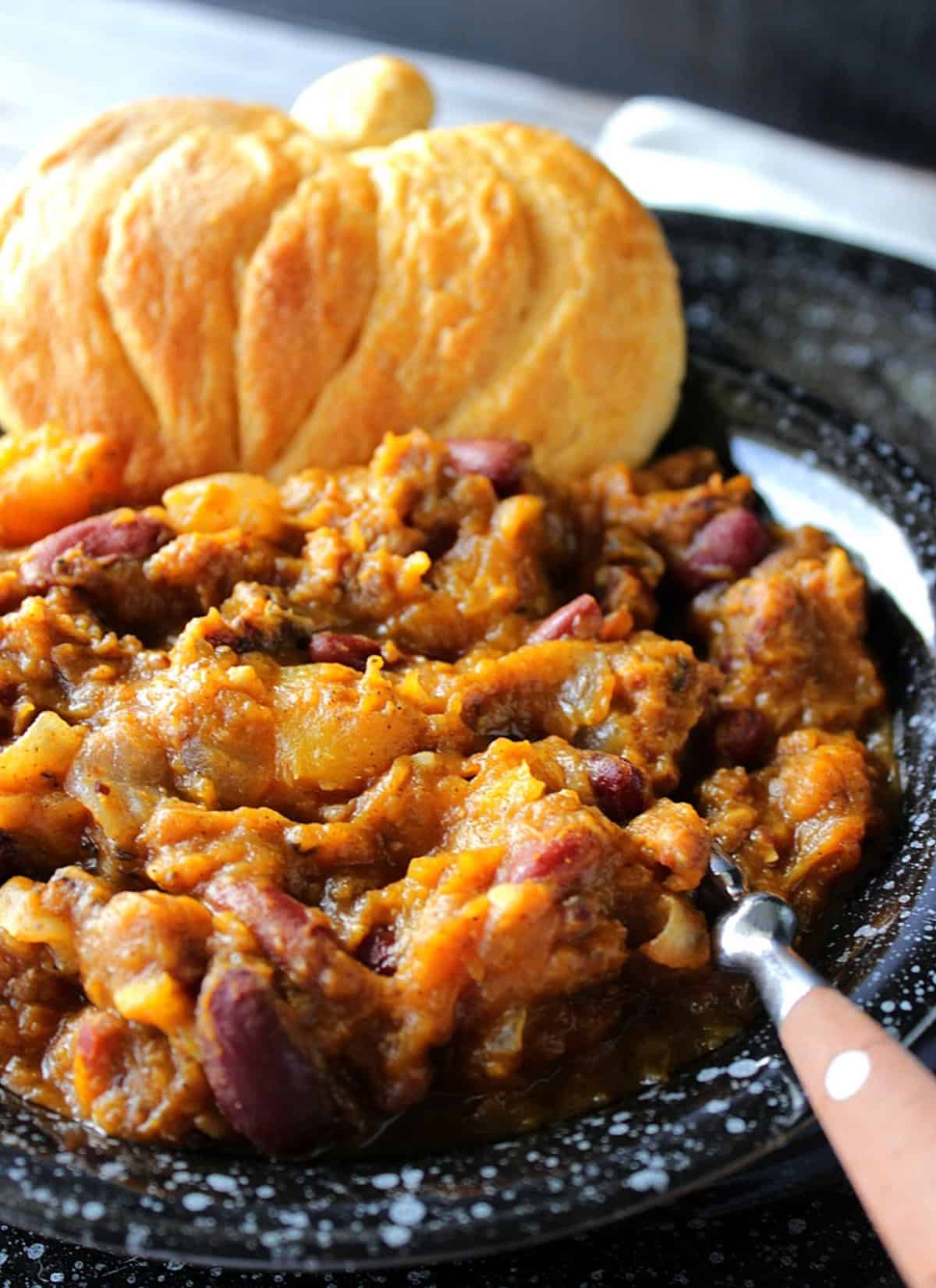 Thick and rich butternut squash chili in a black bowl along with a spoon.