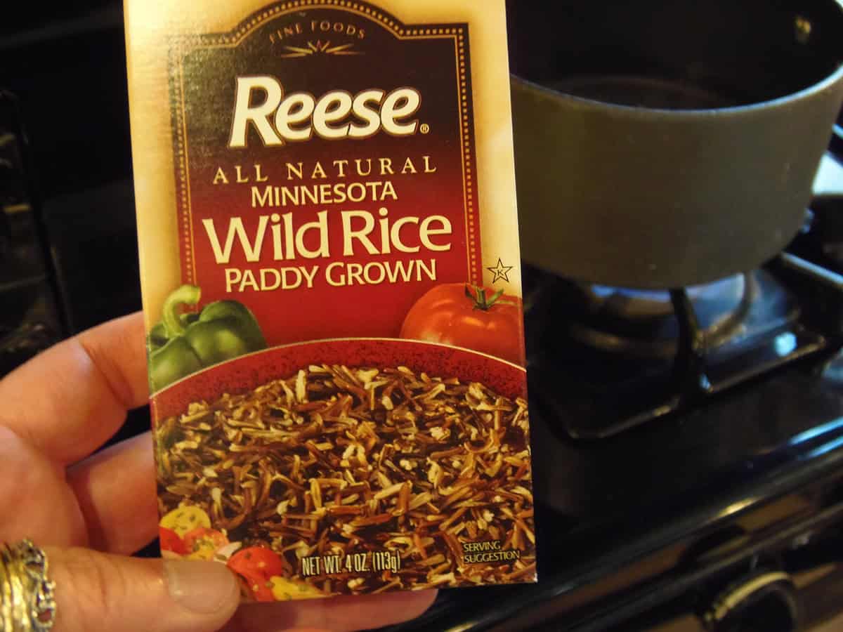 A hand holding a box of uncooked wild rice.