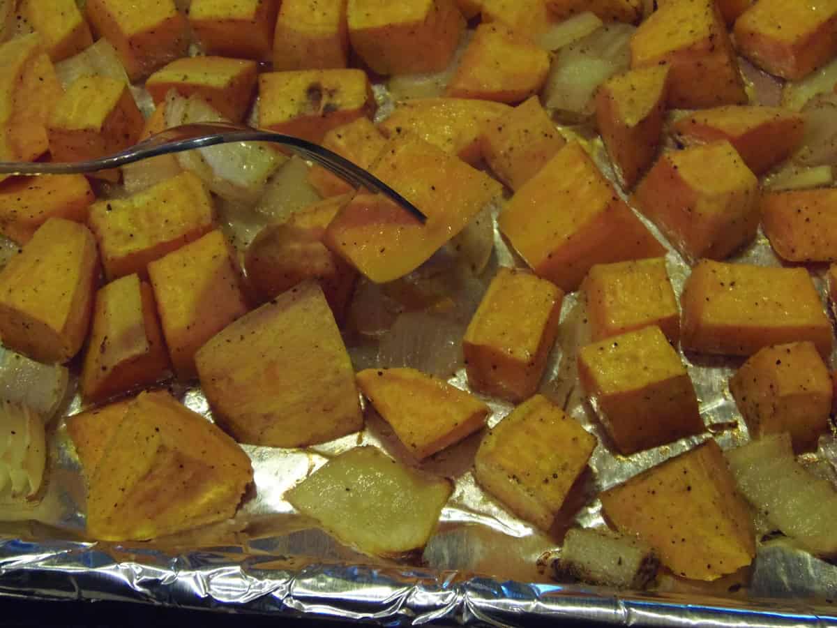 Roasted chunks of sweet potato and onions on a foil lined baking sheet.