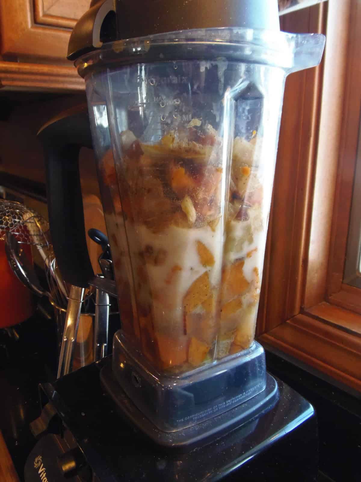 A Vitamix blender with roasted sweet potatoes and onions inside.