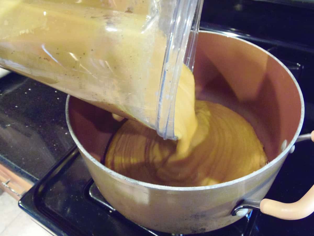 A creamy sweet potato chowder being poured from a blander into a soup pot.