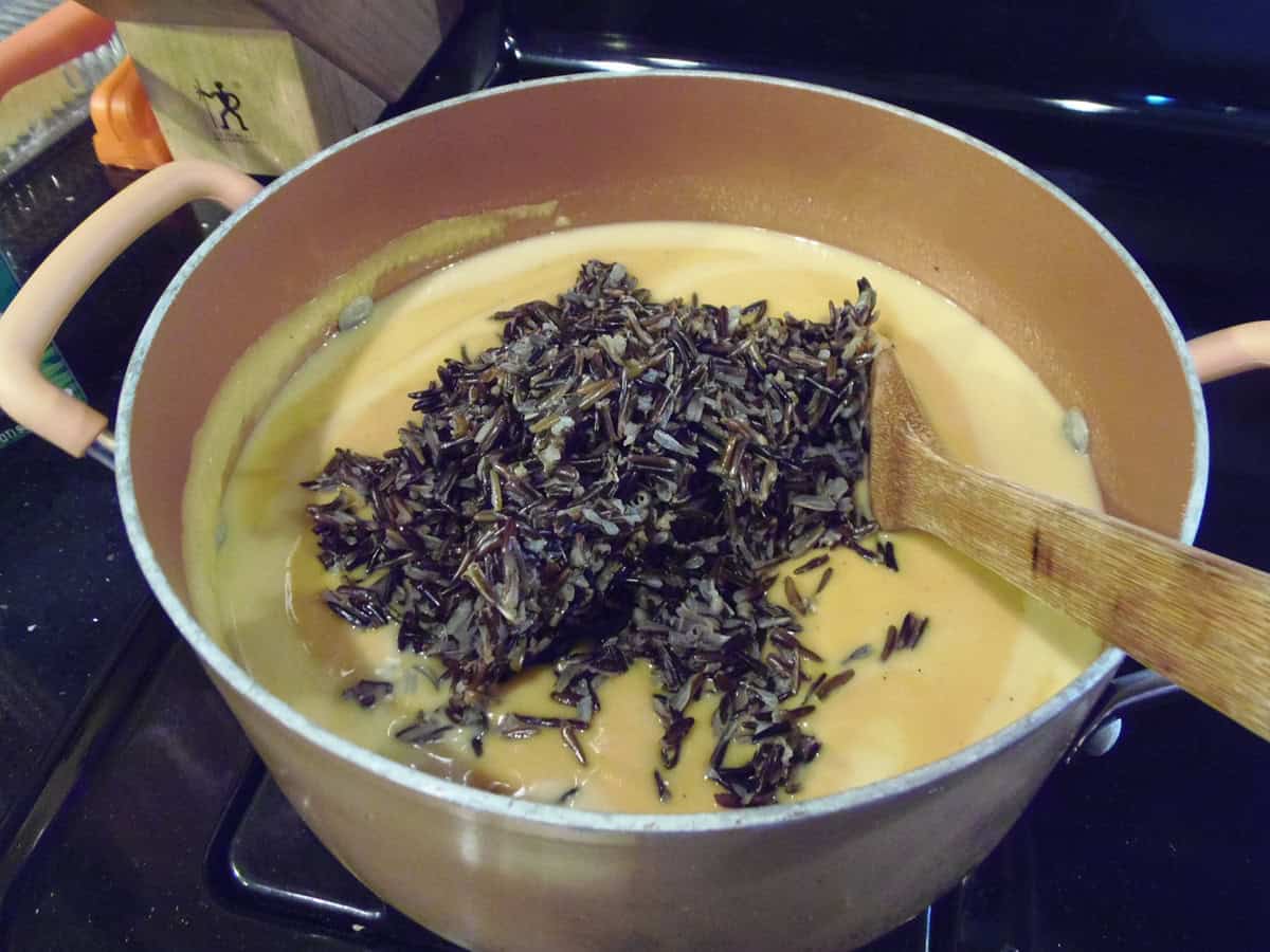 Cooked wild rice in a soup pot full of sweet potato chowder.