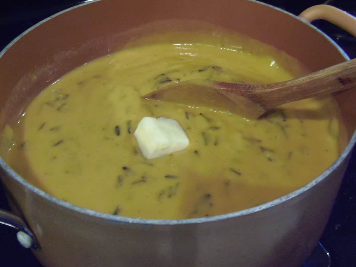 A pat of butter in a soup pot full of sweet potato chowder.