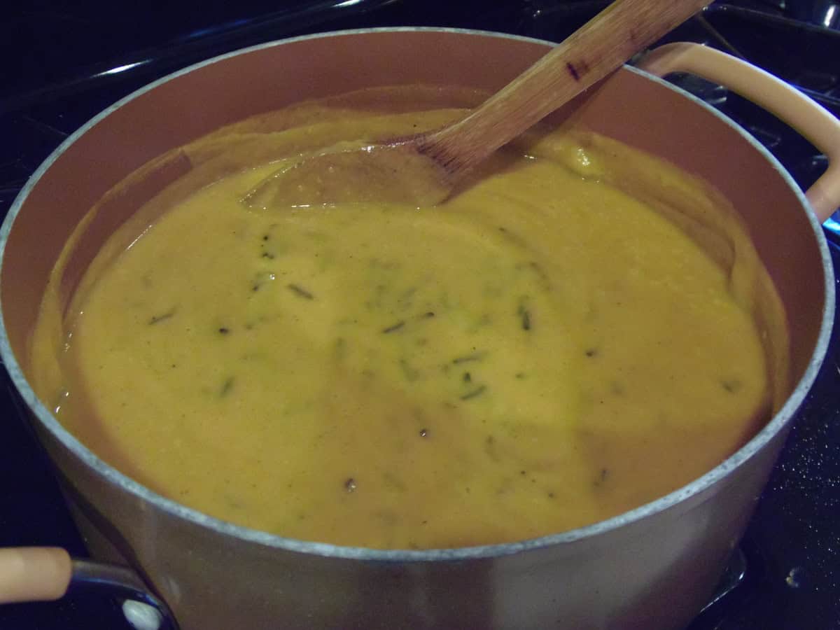 A large copper color soup pot on the stovetop filled with sweet potato chowder.
