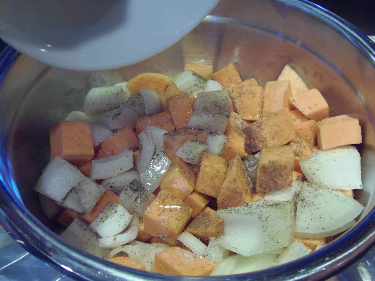 Seasoned chopped sheet potatoes and onions in a bowl with oil.
