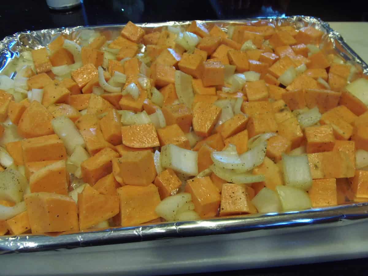 Peeled and chopped sweet potatoes and onions on a foil lined baking sheet.