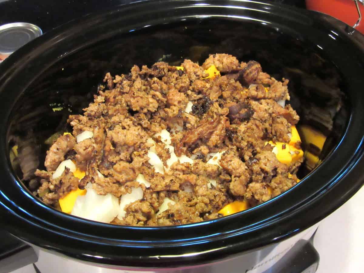 Onion, browned sausage, and butternut squash chunks inside a slow cooker.