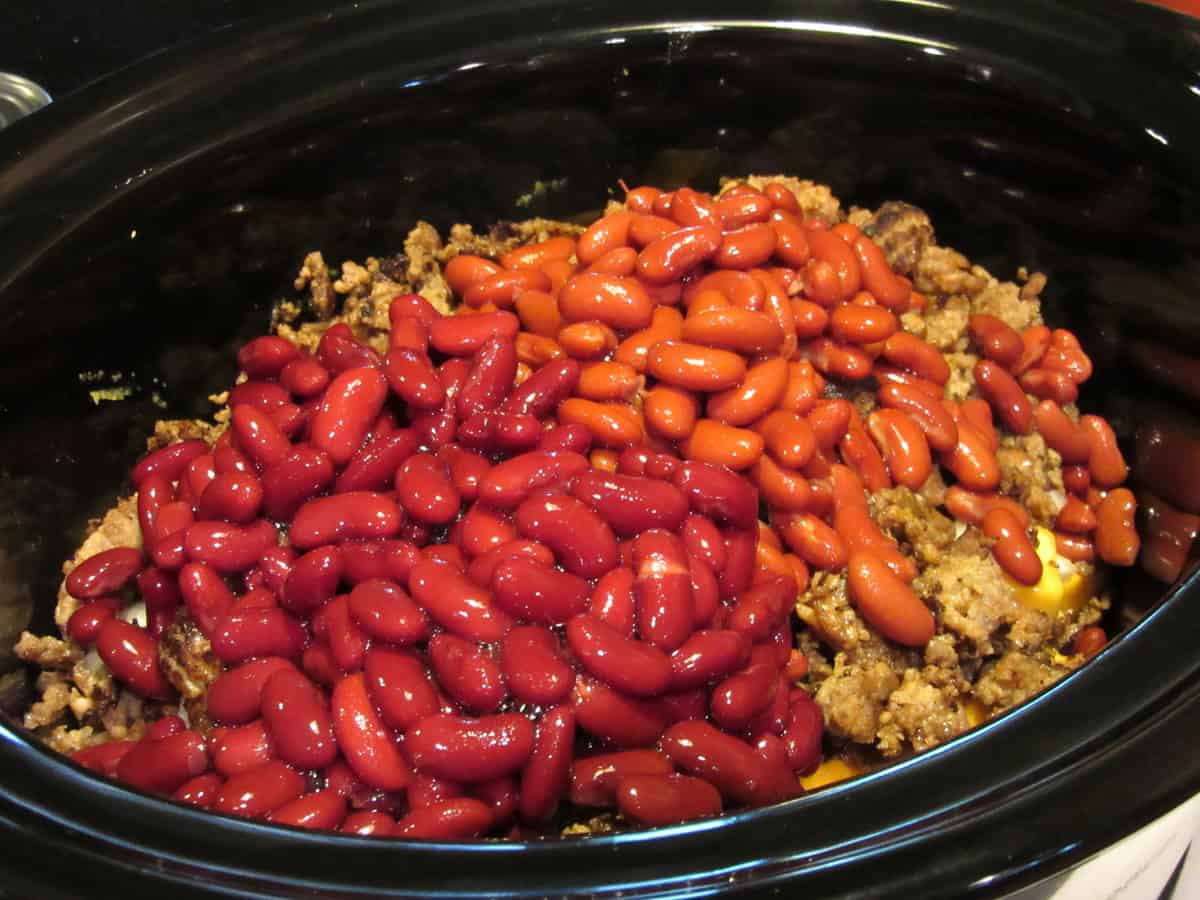 Two colors of drained kidney beans in a slow cooker with browned sausage.