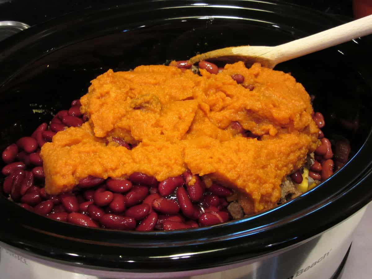 Pumpkin puree, kidney beans and browned sausage inside a slow cooker for making chili.