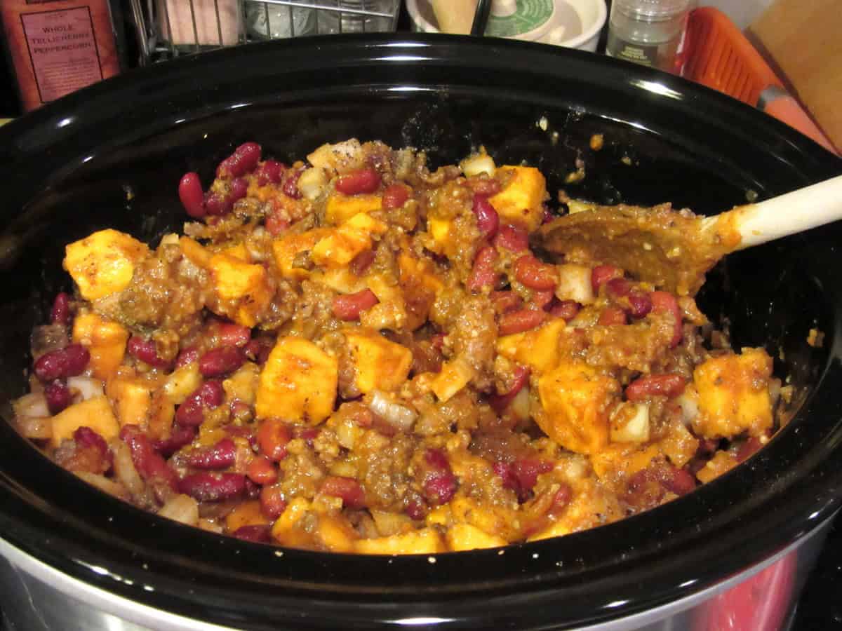 Kidney beans, butternut squash chunks, sausage, and onion inside a slow cooker.