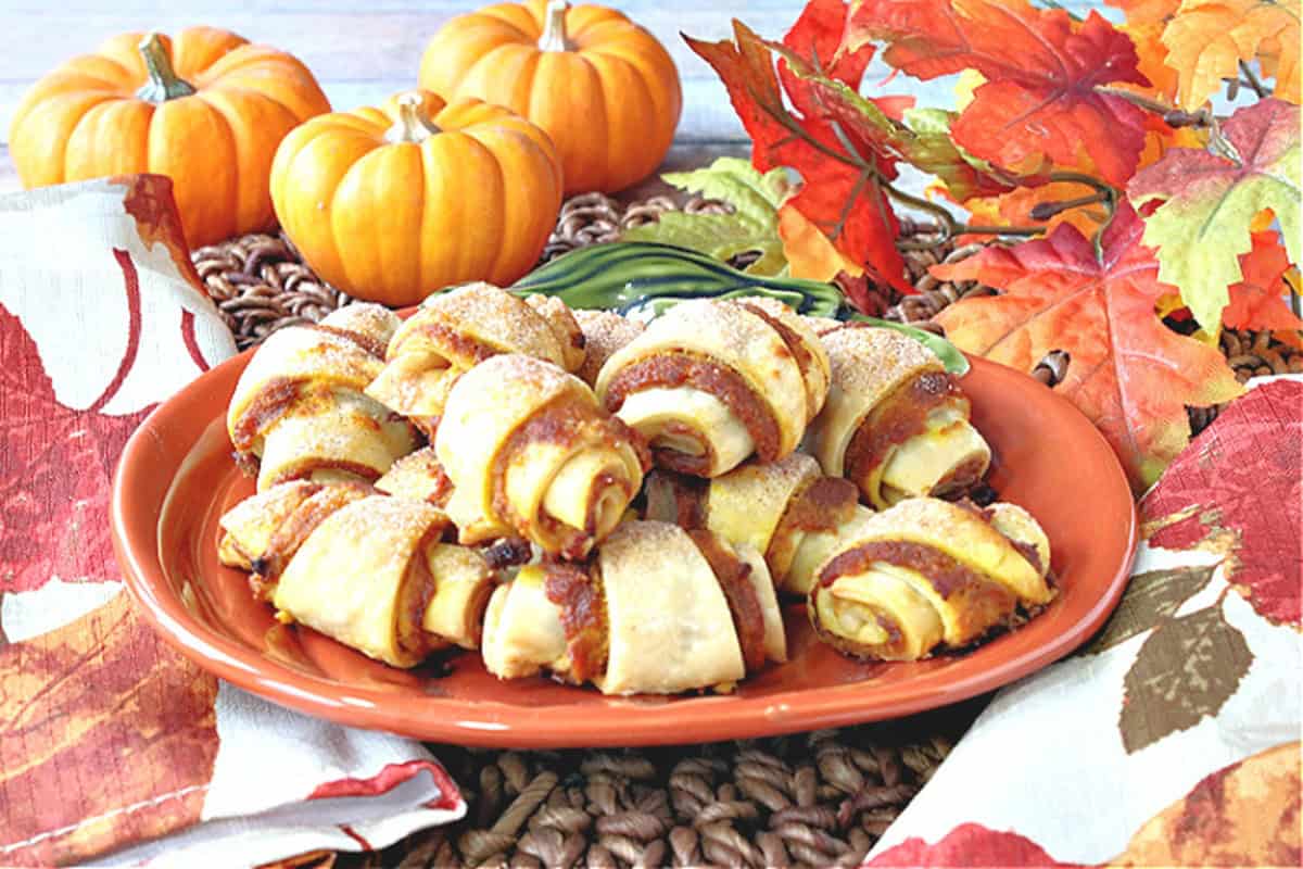 Fall leaves and mini pumpkins in the background of a stack of pumpkin pie bites for dessert.