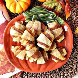 An orange ceramic pumpkin spate on a brown placemat for showcasing a pile of pumpkin pie bites.
