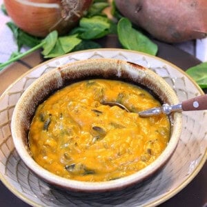 An serving of sweet potato chowder in a brown rustic bowl with a spoon.